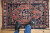 Vintage Senneh rug with madder root and navy geometric Herati design, visible wear.