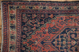 Vintage Senneh rug corner displaying geometric Herati motif, madder root and navy, with visible knot wear.