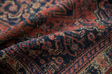 Vintage Senneh rug's worn pile, revealing madder root, navy, and ivory geometric Herati pattern.