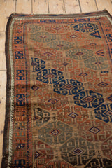 Corner detail of an antique Persian Belouch rug showing geometric guls and a running wave border.