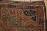 Corner of an antique Belouch rug showing the running wave border and geometric field.