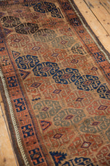 Intricate geometric guls in rust and navy on the low pile of an antique Belouch runner rug.