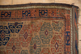 Corner of an antique Belouch rug showing the running wave motif border and dark brown side cord.