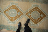Oushak runner's distressed texture, showing ivory, bronze, and slate geometric medallions.