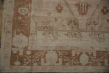 Corner of vintage distressed Oushak rug, showing copper border, ivory motifs, and fringe.