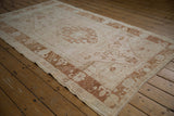 Distressed Oushak rug border featuring coppery abstract florals, pale blush field, and intact side cord.
