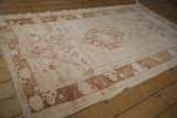Distressed Oushak rug corner detail, pale blush and copper floral border, with fringe.