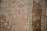 Close-up of distressed vintage Oushak rug pile, showing copper border and pale blush floral vinery.