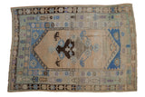 Distressed vintage Oushak rug with asymmetric floral medallion in faded blue, brown, and ivory.