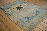Distressed Oushak rug section: asymmetric medallion, plant motifs, and borders in muted blue, ivory, brown tones.