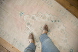 The even, low-pile wear of a distressed vintage Oushak rug in blush, ivory, and green.