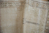 Folded distressed Oushak rug pile showing ivory, beige tones, and geometric border.