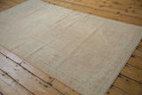 Distressed Oushak rug with even wear, featuring pale green patterns and intact selvage.