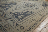 Distressed Oushak carpet corner detail, displaying geometric floral motifs in dusty navy and ivory.
