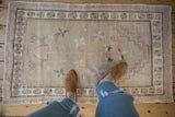 Distressed Oushak rug corner: beige and soft pink pinwheel floral border with even wear.