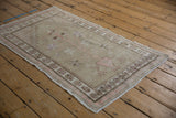 Distressed Oushak rug corner with beige field, pink stepped contour, and pinwheel floral border.