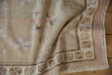 Distressed pile texture and pinwheel border detail of vintage Oushak rug in beige and mauve.