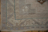 Distressed Oushak rug corner: beige and pale mauve geometric border, turquoise line, and pile wear.