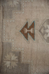 Brown and turquoise geometric motif on the distressed beige field of a vintage Oushak rug.