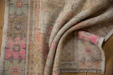 Distressed Oushak rug texture with vibrant pink and muted orange geometric patterns.