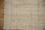 Beige and ivory Oushak rug texture, showing distressed pile with wear and selvage.