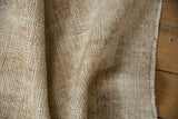 Distressed beige and ivory Oushak rug pile revealing knot heads and intact selvage.