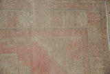 Close-up of distressed Oushak rug texture with blush pink and pale turquoise patterns, showing even wear and faint foundation.
