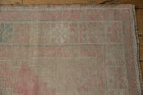 Distressed Oushak rug corner showing worn pile texture, blush pink, and pale turquoise motifs.