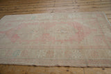 Angled view of a distressed vintage Oushak rug with blush pink medallion and pale turquoise accents.