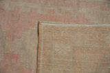 Folded vintage Oushak rug revealing distressed blush pink pile and hand-knotted foundation.