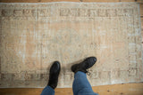 Vintage distressed Oushak rug's muted beige and silver pattern with visible low pile, featuring boots for scale.
