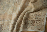 Distressed Oushak rug with beige, silver, and sandalwood tones, showing wear and geometric border.