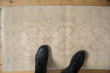 Distressed vintage Oushak mat, beige and ivory with subtle green floral motifs and wear.