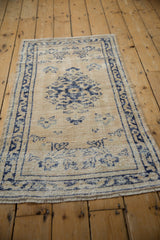 Distressed ivory Oushak rug with navy floral sprays, visible knot heads, and fringe.