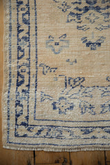 Distressed vintage Oushak rug corner, highlighting worn ivory pile, navy blue border, and short fringe.