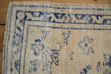 Distressed Oushak rug corner: fringed edge, ivory pile, navy border, and even wear.