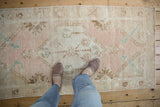Distressed Oushak runner's worn pile texture with dusty rose, ivory, and pale aqua floral motifs.