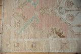 Distressed Oushak rug corner, showing worn pile, exposed foundation, and dusty rose, aqua, beige motifs.