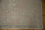 Distressed Oushak rug corner showing dusty green meandering vine border and intact selvage.