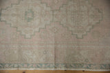 Distressed Oushak rug close-up: faded blush, dusty sea foam geometric border, even wear.