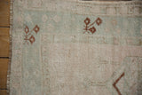 Distressed vintage Melas rug detail with pale green, beige pile, copper motifs, and fringe.