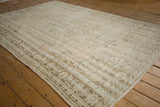 Distressed Oushak carpet corner with faded ivory and brown floral vines and textured border.
