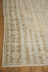 Distressed Oushak rug corner showcasing worn beige patterns, intact side selvage, and fringe.