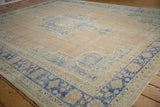 Corner of a distressed Oushak carpet featuring worn pale denim blue floral border and dusty blush field.