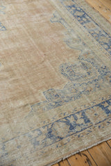 Distressed vintage rug showing abrash, faded dusty blush, pale blue border detail, and fringe.