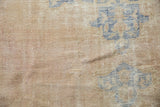 Distressed vintage Oushak rug showing worn texture, faded blue designs, and dusty rose field.