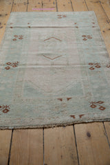 Distressed pale mint and ivory pile of the Melas rug with rust geometric patterns and fringe.
