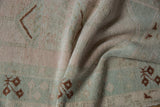 Distressed Melas rug pile texture in softened blush, pale mint, and geometric brown.