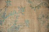 Worn pile of a distressed Oushak with faded teal floral motifs on antique ivory.
