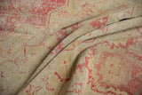Texture of a vintage Oushak carpet, folded to reveal cherry red patterns on an antique ivory ground.